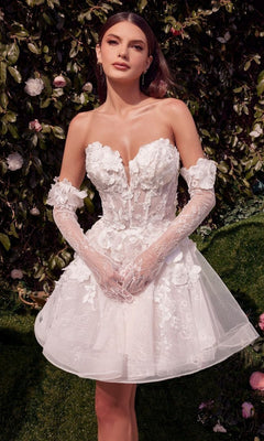 A woman stands outdoors before foliage, wearing the Andrea and Leo WL020 short white party dress with delicate floral appliques and matching lace gloves.