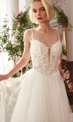 A woman in the Andrea and Leo WL029 long wedding dress with a sleeveless lace corset bodice stands indoors near greenery and a mirror.