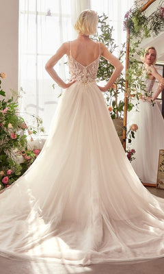 A woman wearing the Andrea and Leo WL029 long wedding dress with a sleeveless lace corset bodice and flowing tulle A-line skirt stands facing away, gazing into a flower-framed mirror lit by natural light.