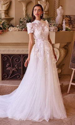 A woman wearing the Andrea and Leo WL040 long wedding dress with a fitted lace design and sweetheart neckline stands indoors near decorative columns and floral arrangements.