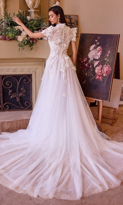 A woman, her back to the camera, stands indoors near a fireplace and floral painting wearing the Andrea and Leo WL040 long fitted lace wedding dress with a sweetheart neckline.
