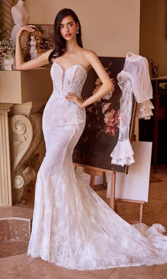 A woman wearing the Andrea and Leo WL042 long wedding dress with a fit-and-flare silhouette stands indoors beside a floral painting and an easel draped with a lace veil.