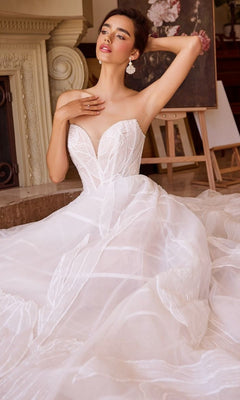 A woman wears the Andrea and Leo WL043 Long Wedding Dress, featuring a strapless design with leaf-patterned details and a tulle A-line skirt, as she sits on the floor and poses with one arm raised near her head.