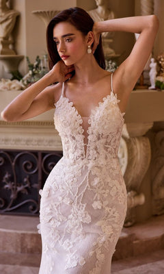 A woman stands indoors before a decorative fireplace, wearing the Andrea and Leo WL053 long wedding dress—a sleeveless lace gown with floral applique, thin straps, and an elegant adjustable lace-up back for a perfect fit.