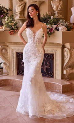 A woman in the Andrea and Leo WL053 long wedding dress with floral lace applique and an adjustable lace-up back stands indoors by a fireplace adorned with flowers and classical sculptures.