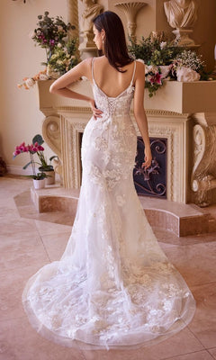 A woman in the Andrea and Leo WL053 Long Wedding Dress, featuring a fitted sleeveless lace design and adjustable lace-up back, stands indoors facing a fireplace decorated with flowers.