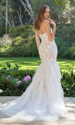 Woman showing the back of a white wedding dress she's wearing standing in a garden setting