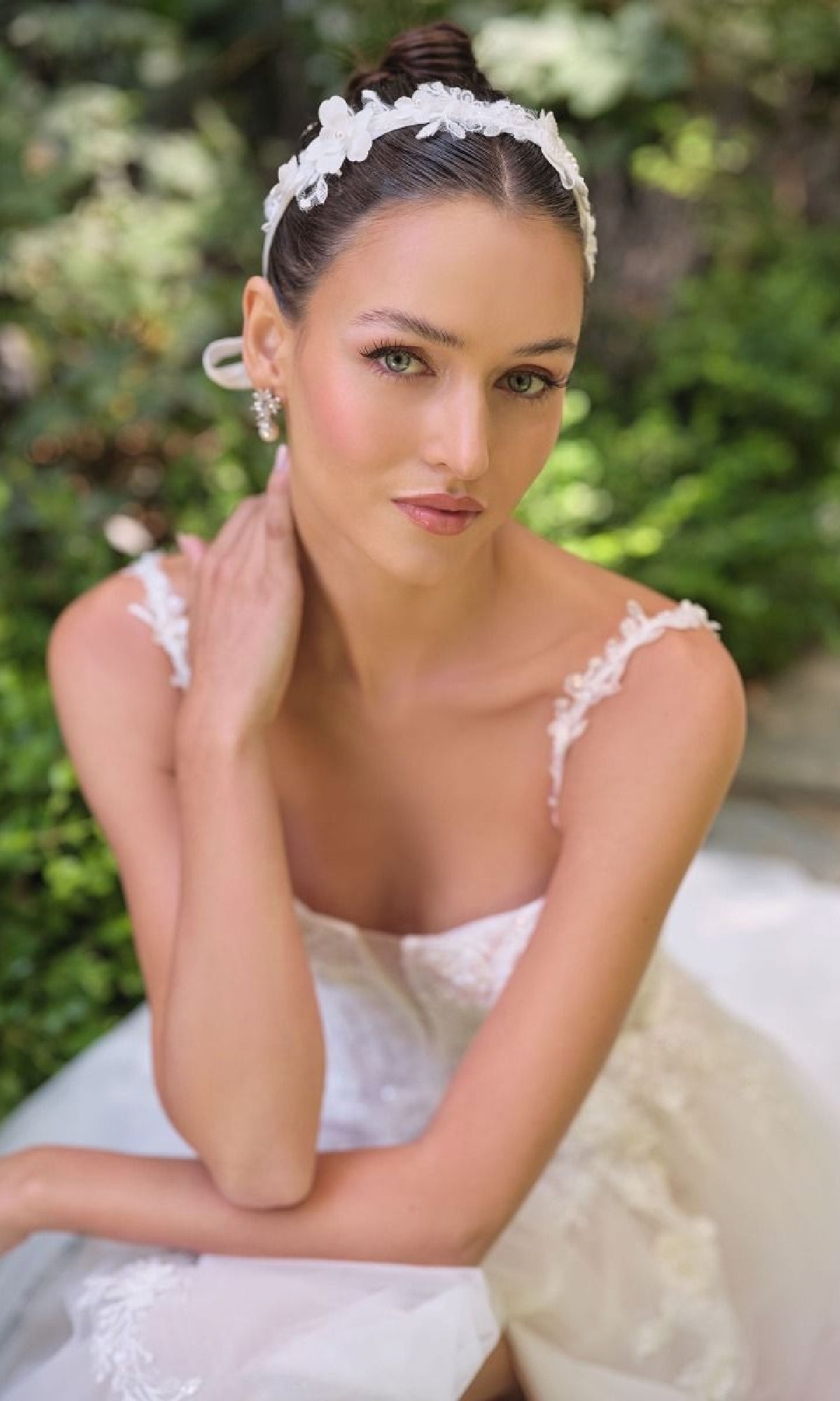 Bride in a white dress with a floral headband sitting outdoors.