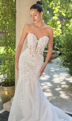 A woman stands outdoors by greenery and a column, wearing the Long Wedding Dress: Andrea and Leo WL065—an elegant strapless lace mermaid gown with floral embroidery.
