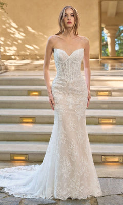 A woman stands on stone steps wearing the Andrea and Leo WL071 long wedding dress, featuring a strapless sweetheart neckline, white lace fabric, and a long train.