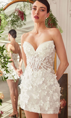 A woman wears the Short White Dress: Andrea and Leo WL083 with 3D floral appliques and sheer panels, standing before a mirror with greenery and flowers in the background.