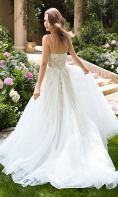A woman wearing the Andrea and Leo WL087 long wedding dress with a lace back stands in a garden of blooming flowers, her white A-line gown adorned with delicate lace appliques.