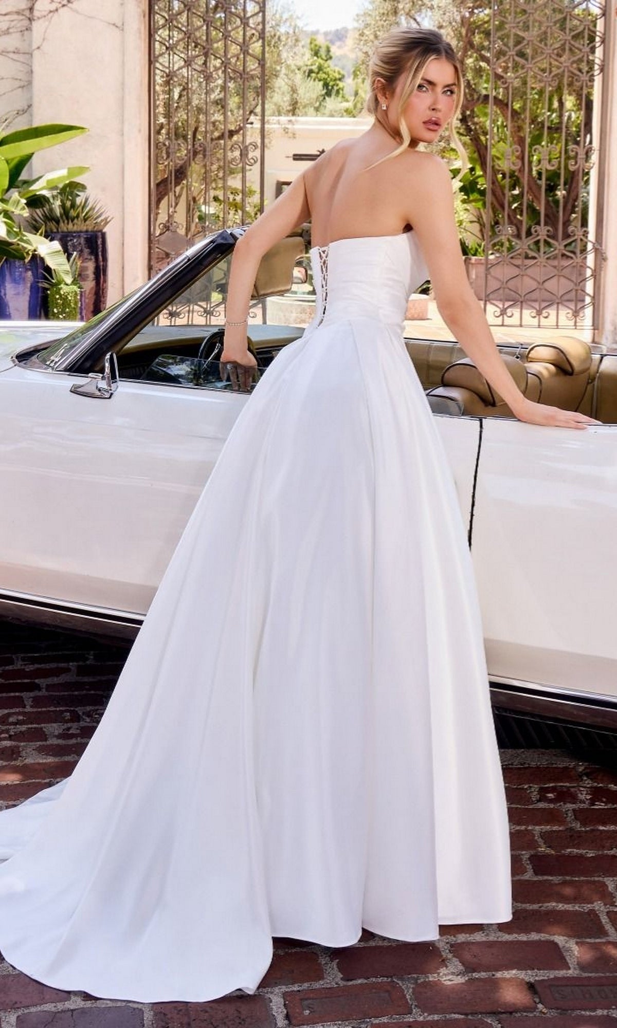 Wearing the Ladivine WN015 A-Line Long Classic White Dress with a sweetheart neckline and strapless design, a woman stands beside a white convertible car, looking over her shoulder.