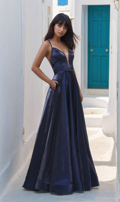 Woman in a La Femme 25670 Long Prom Dress featuring a plunging neckline and open back stands on a sunlit narrow street with white walls and a turquoise door in the background.