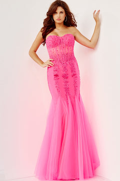 A woman wears the Long Strapless Sweetheart Jovani Prom Dress 5908, a floor-length, bright pink mermaid gown with sequin embellishments, standing against a white wall.