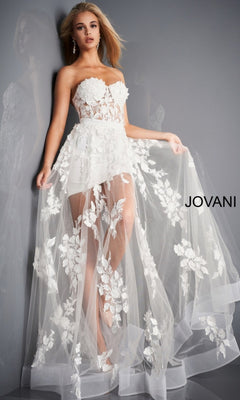 A woman models the Jovani Strapless Sweetheart Sheer Corset Prom Dress, a strapless white gown with a sheer floral overlay and short lining, against a gray background. "JOVANI" is displayed on the right side.