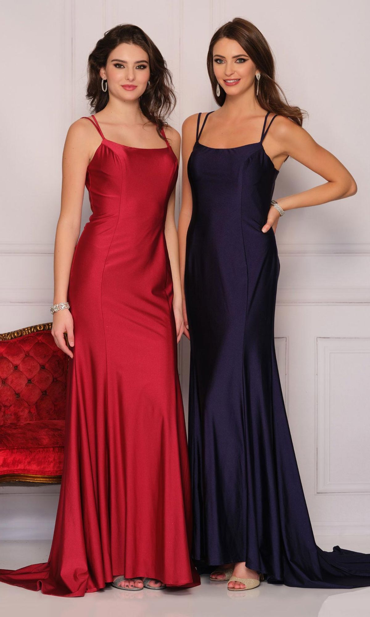 Two women stand side by side in a formal indoor setting, both wearing elegant long dresses; one wears a red gown, while the other models a dark blue Open-Back Long Formal Prom Dress by Dave & Johnny.