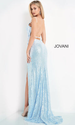 A woman stands against a white background wearing a light blue Long Sequin Jovani Prom Dress with appliques, featuring a backless design and long train. The word "JOVANI" appears on the wall.