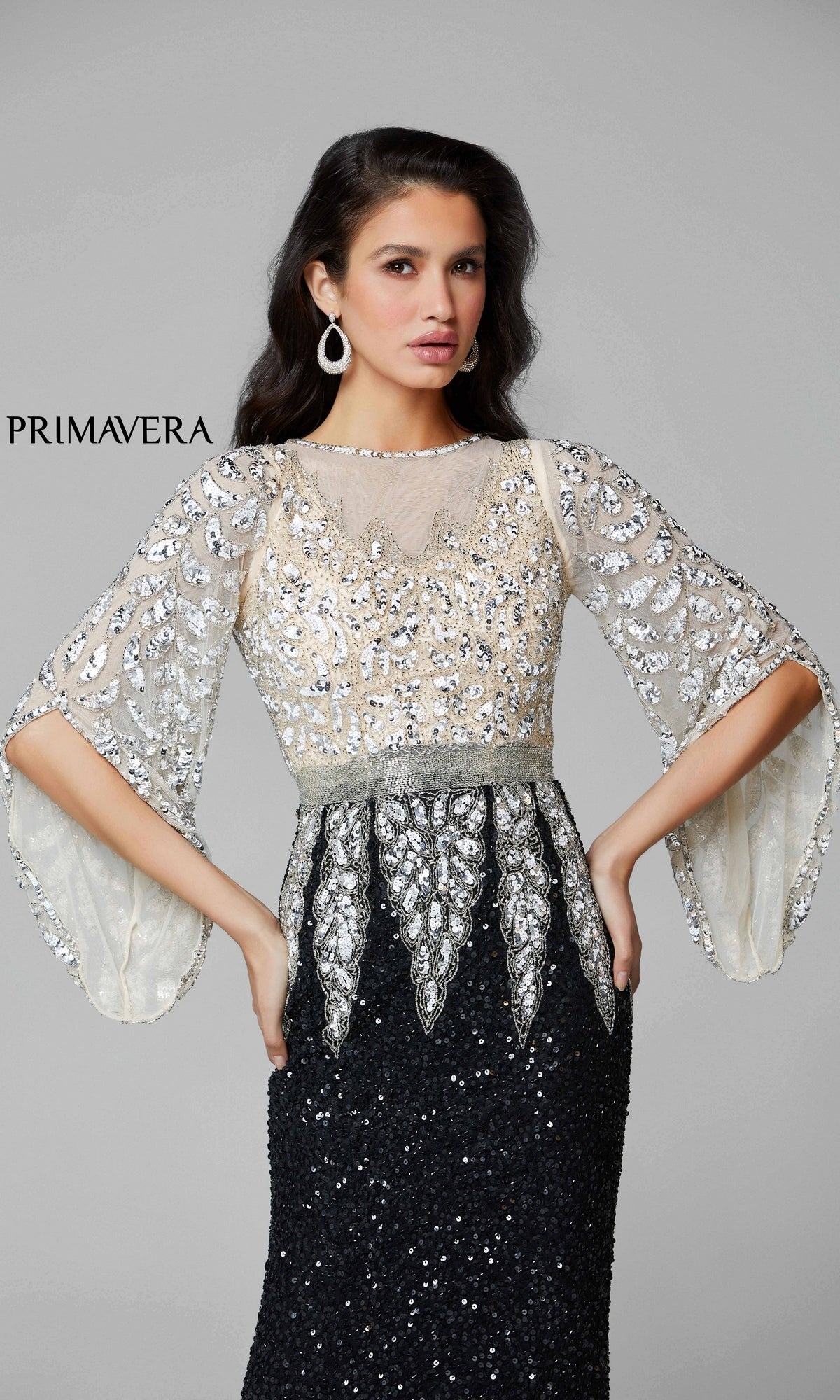 A woman poses with hands on hips in the Bell-Sleeve Long Beaded Evening Gown 1424, featuring black and silver beadwork, sheer embellished sleeves, and a sequin skirt. 