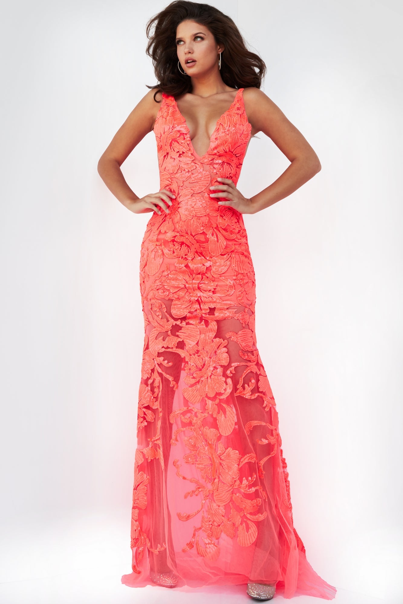 Woman in a sleeveless, floor-length tangerine Jovani Embroidered Long Prom Dress with sequins and a deep V-neckline, standing with hands on hips against a plain background.