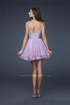 A woman in a studio wears the La Femme Short Tiered Party Dress with Beads in light purple, featuring a beaded sweetheart bodice, paired with silver bracelets and high heels.