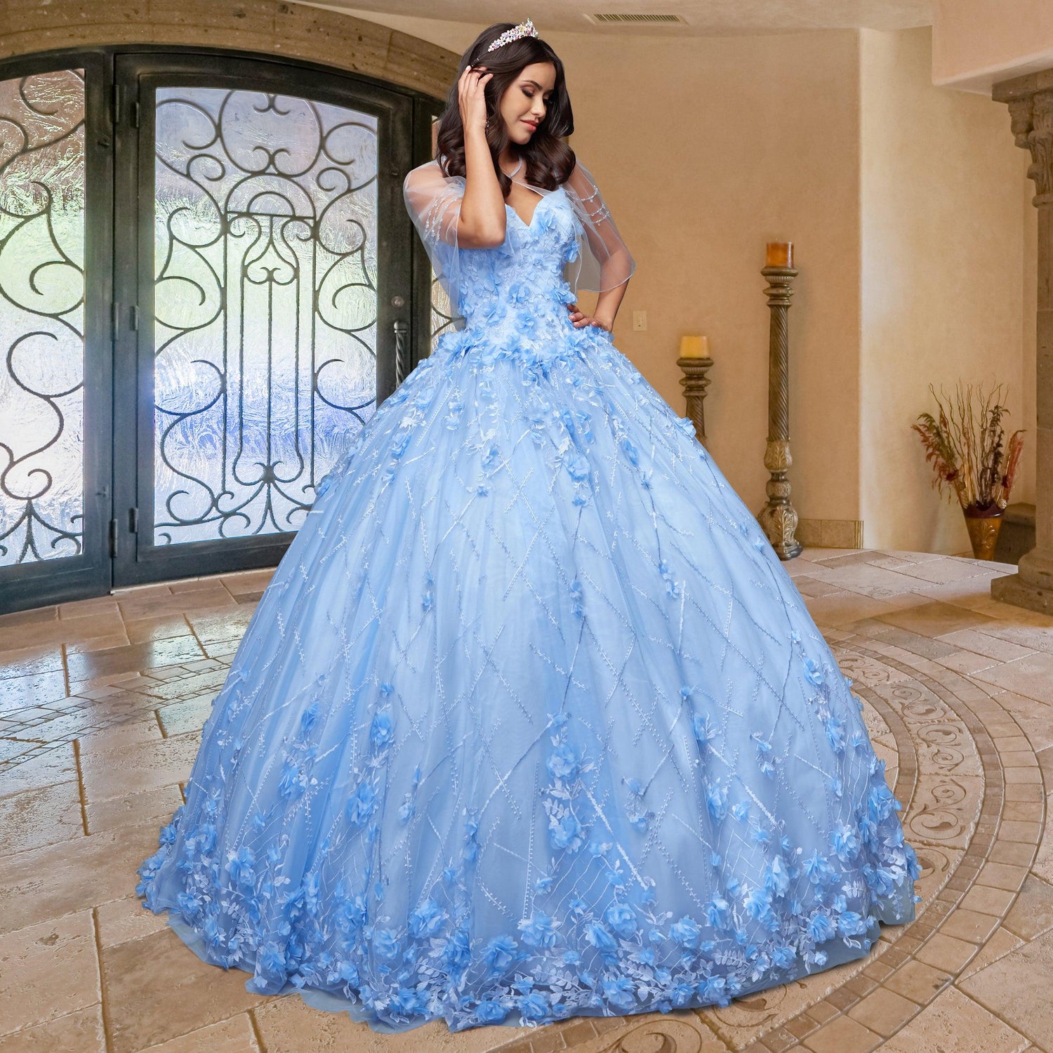 A woman stands indoors near ornate double doors and decorative columns, wearing the Quinceañera Sample Dress QF105—a light blue cold-shoulder gown with floral details.