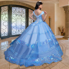A young woman wears the Quinceañera Sample Dress QF104 and a tiara, standing indoors on a tiled floor facing ornate glass doors with her back to the camera.