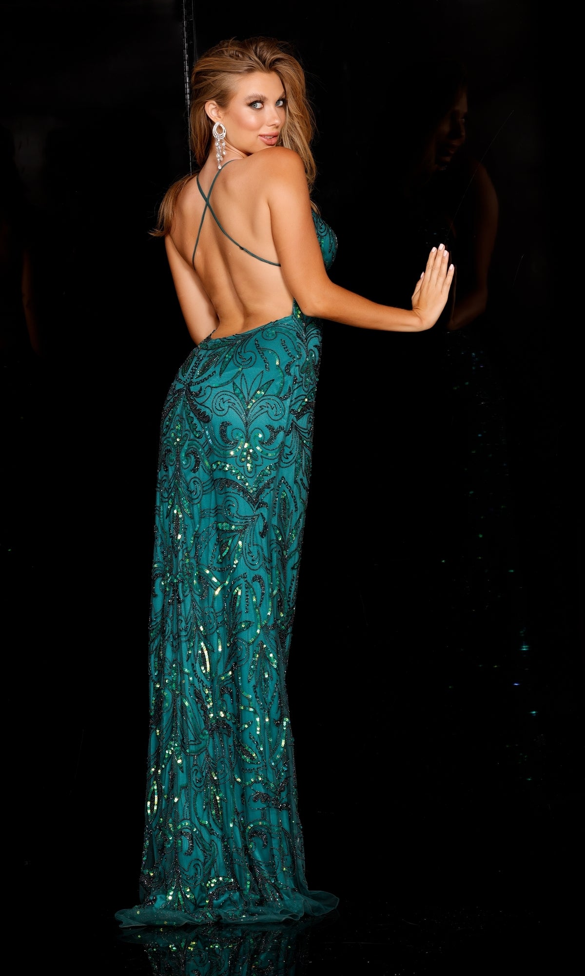 A woman in the Aleta Empire-Waist Long Sequin-Print Prom Dress, featuring a teal, floor-length sequin design and open back, stands before a dark background, looking over her shoulder.