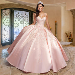 A young woman smiles in an ornate, sunlit room while wearing the Quinceañera Sample Dress QF106—a pink, v-neck gown with sparkling embellishments and a tiara—standing near wrought iron doors and decorative columns.