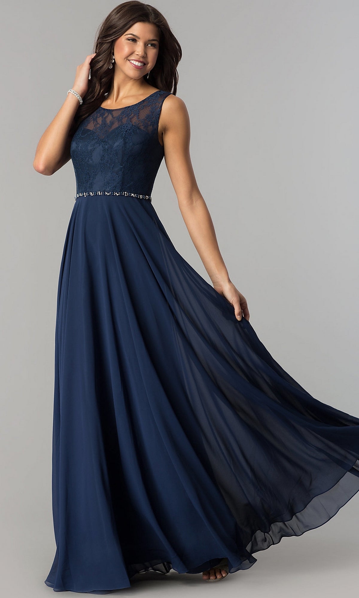 A woman poses against a plain background in the Lace-Bodice Long Chiffon Illusion-Neck Prom Dress, featuring a sleeveless navy blue design with a lace bodice and flowing floor-length skirt.