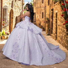 A woman in the Quinceañera Sample Dress QF115 and a tiara stands on a narrow cobblestone street lined with stone buildings and flowers.