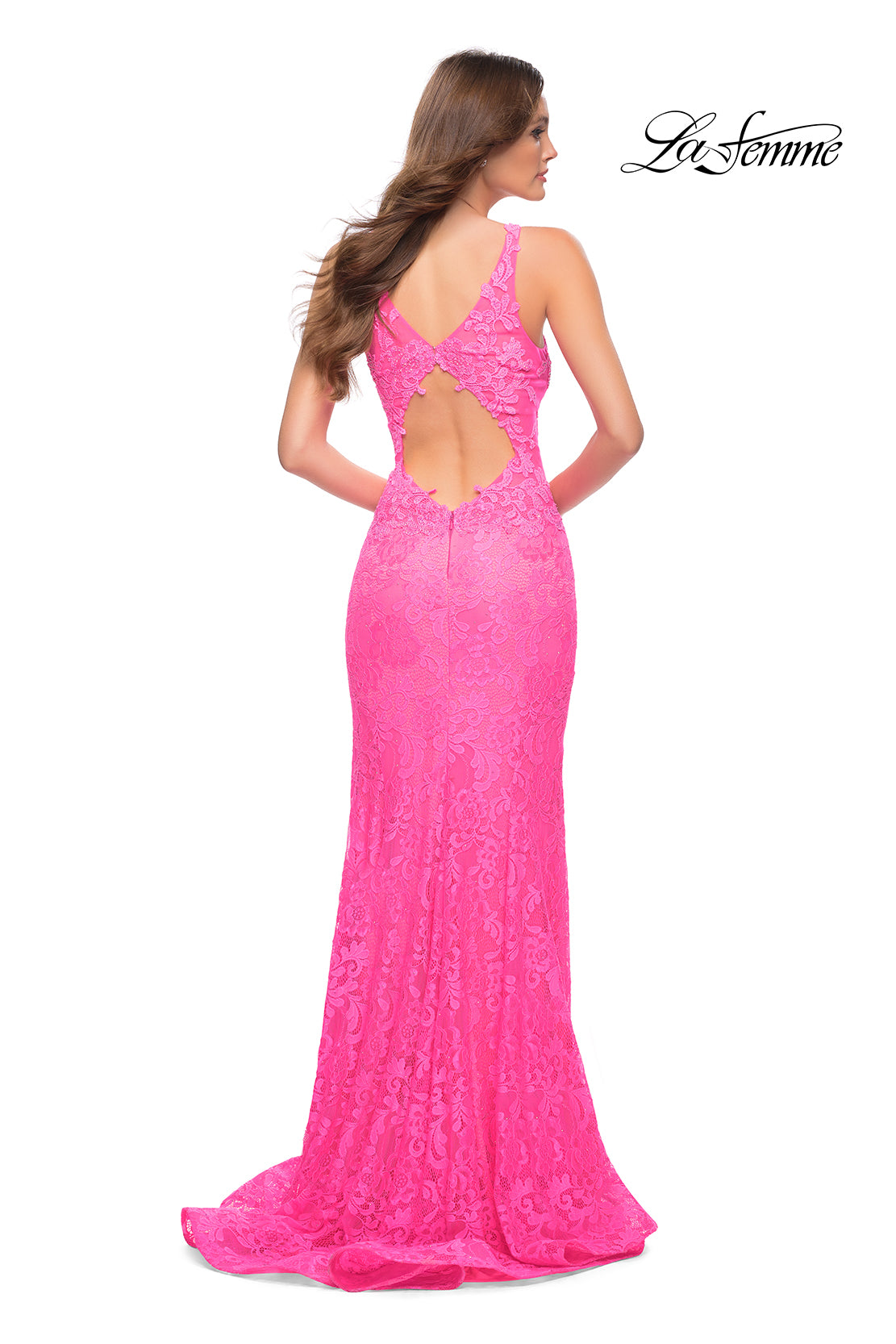 A woman stands facing away, wearing the Deep V-Neck Long Lace Prom Dress: La Femme 29978 in bright pink with an open back and floor-length hem. The 