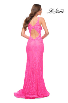 A woman stands facing away, wearing the Deep V-Neck Long Lace Prom Dress: La Femme 29978 in bright pink with an open back and floor-length hem. The "La Femme" logo appears in the top right corner.