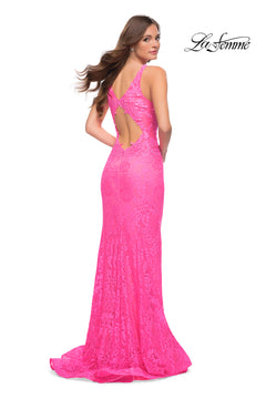 A woman stands, looking over her shoulder, wearing the Deep V-Neck Long Lace Prom Dress (La Femme 29978) in bright pink with lace details, open back, and mermaid silhouette. The La Femme logo appears in the top right corner.