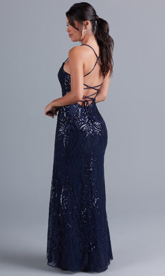 A woman wears the PromGirl Statement-Back Long Sequin Prom Dress in navy blue, featuring spaghetti straps and an open crisscross lace-up back, standing against a plain gray background.