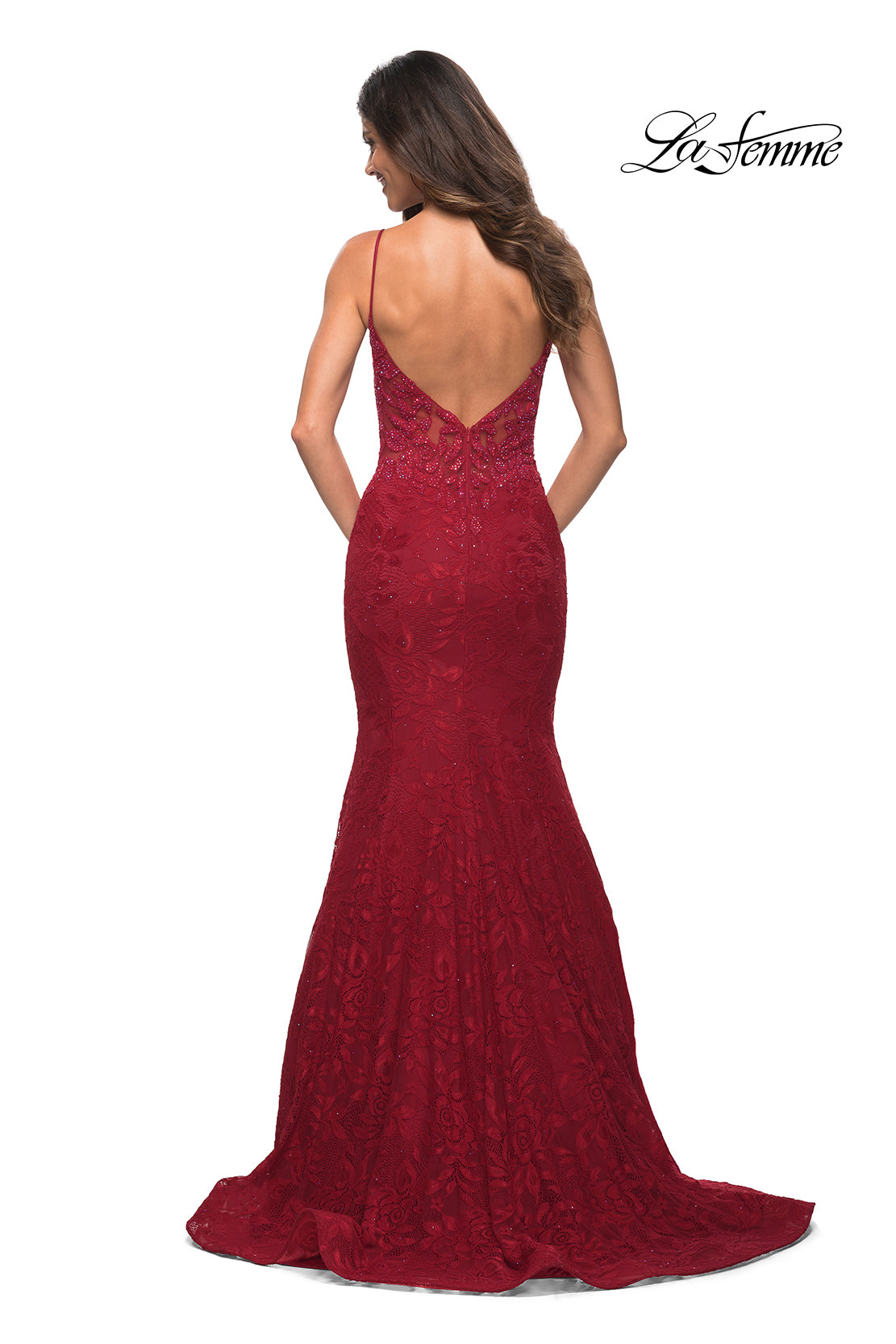 A woman models the La Femme Lace Sheer-Waist Long Mermaid Prom Dress in deep red with thin straps and a low V-back, posing against a white background. The 