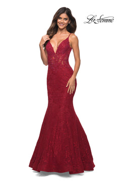 Woman poses and smiles in a sleeveless, deep v-neck, floor-length red La Femme Lace Sheer-Waist Long Mermaid Prom Dress with floral lace patterns, set against a white background. "La Femme" logo appears in the top right.