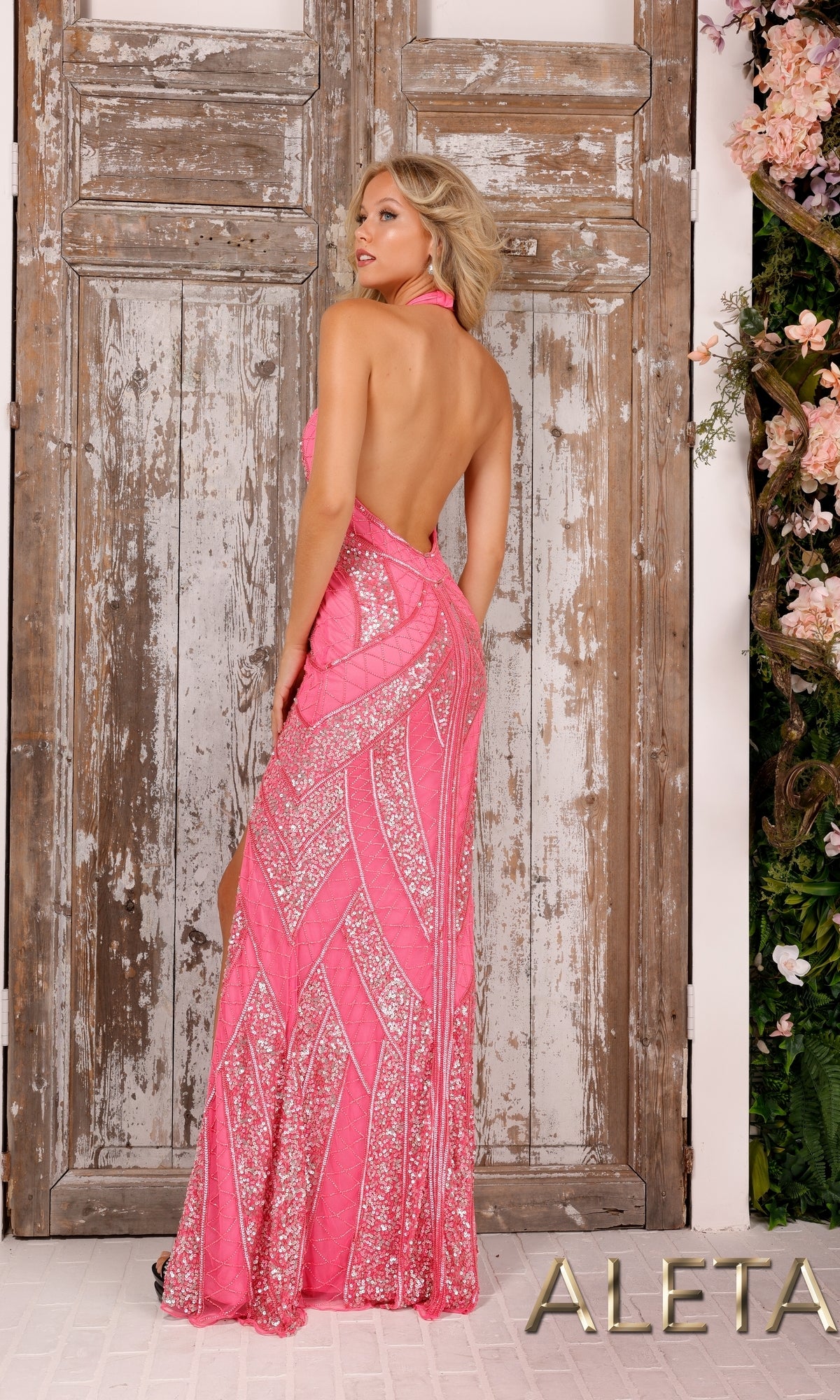 A woman stands before rustic wooden doors, wearing the Beaded Long Halter Formal Dress with Open Back. This elegant pink gown has sequined beading, a halter neck, and an open back. The product name appears at the bottom right.