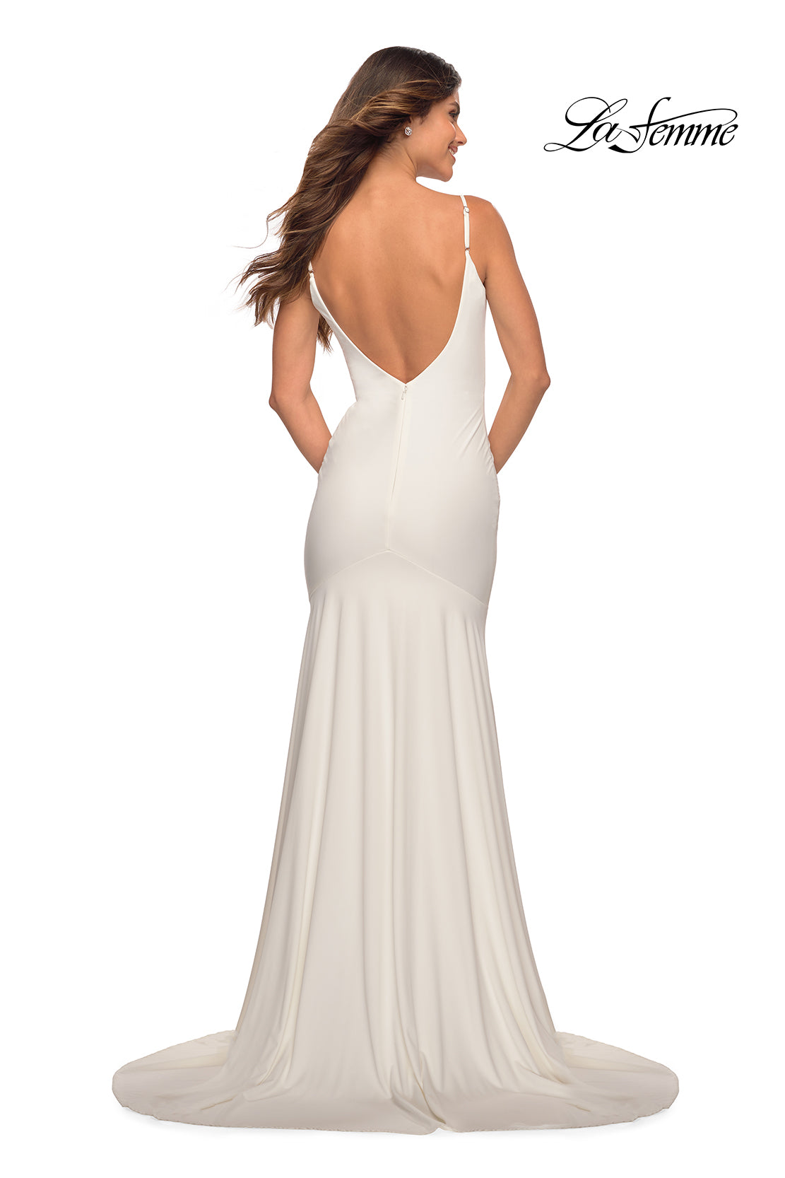 A woman in a white, floor-length La Femme Backless Long Prom Dress with a train, deep V-back, and thin straps stands with her back to the camera. The La Femme logo appears in the upper right corner.
