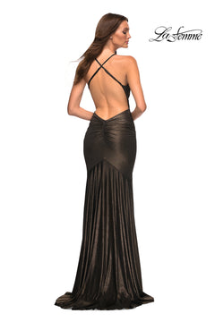 A woman stands facing away in a floor-length metallic black La Femme Open-Back Long Metallic Prom Dress with crisscross straps. Perfect as a long prom dress. "La Femme" logo appears in the top right corner.