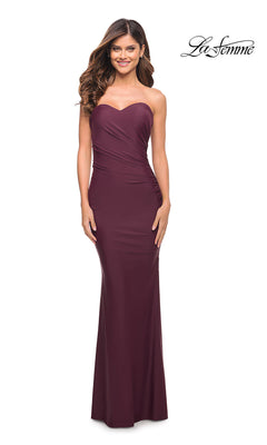 A woman models the Strapless La Femme Long Sweetheart Prom Dress—a floor-length burgundy gown with a fitted bodice and gentle waist gathering—standing against a white background featuring the "La Femme" logo.