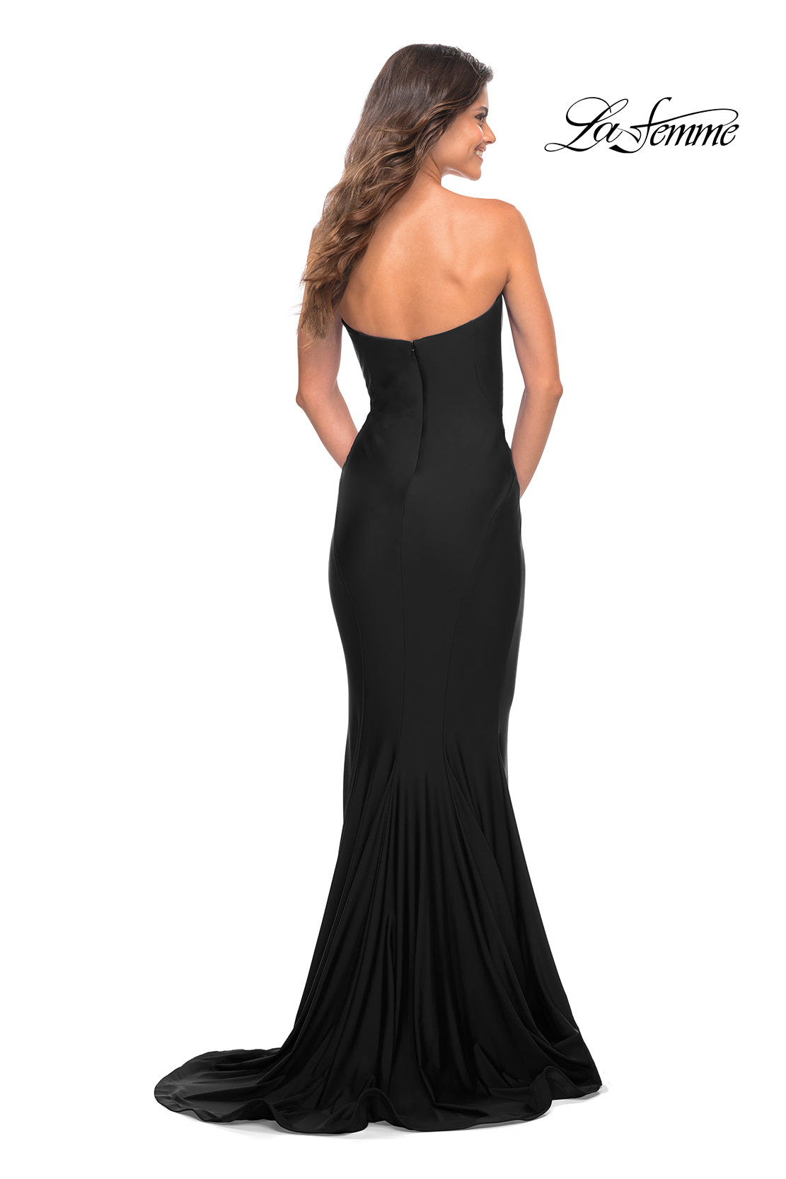 A woman stands with her back to the camera in a black La Femme Simple Mermaid Strapless Formal Dress, featuring a fitted bodice and flowing train. The 