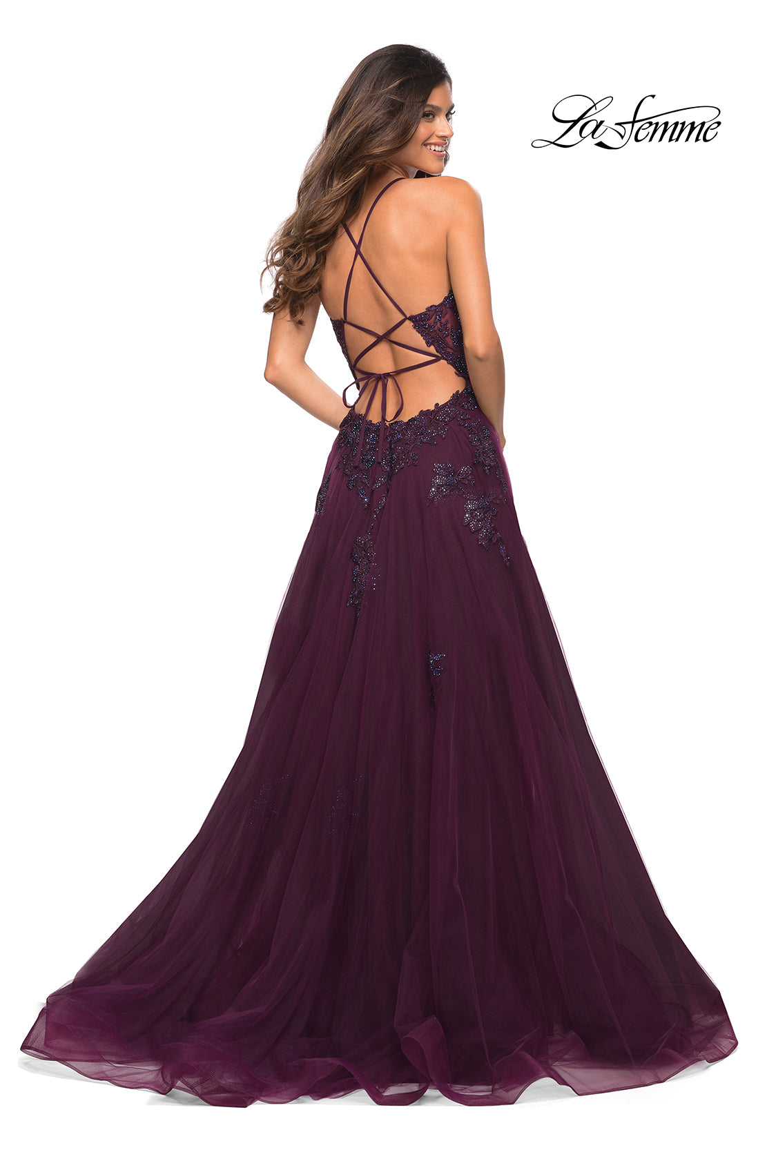 A woman wears the La Femme Open-Back Long Ball Gown with Lace, a floor-length deep purple dress featuring lace embellishments, lace-up detailing, an open back, and a flowing tulle skirt for an elegant A-line silhouette.