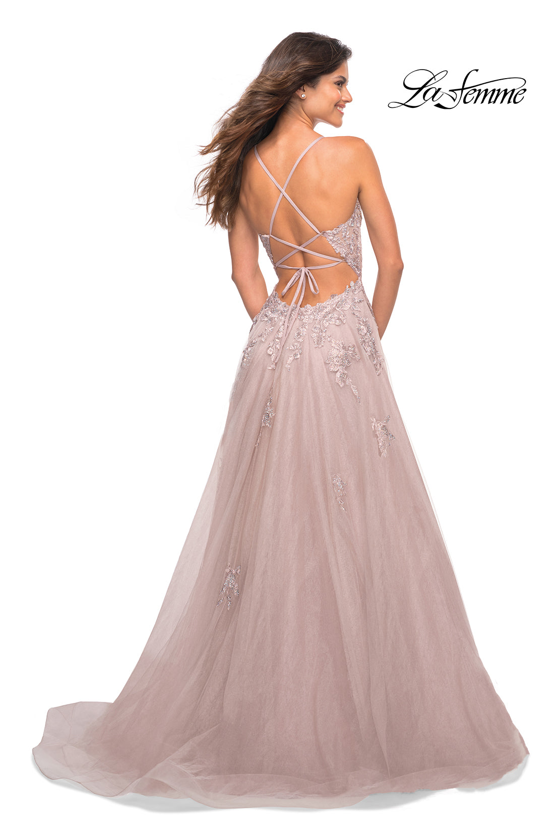 A woman wearing a La Femme Open-Back Long Ball Gown with lace stands smiling over her shoulder.