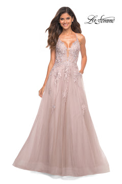 A smiling woman wears the La Femme Open-Back Long Ball Gown with Lace in blush pink, featuring a deep V neckline, thin straps, and delicate lace embroidery. The "La Femme" logo is displayed in the top right corner.