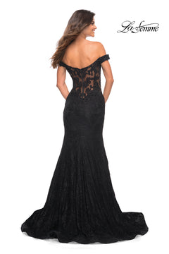 Woman in a La Femme Off-the-Shoulder Long Lace Prom Dress, featuring a sheer back and floral details, stands with her back to the camera—an elegant floor-length gown perfect for prom or any formal event.