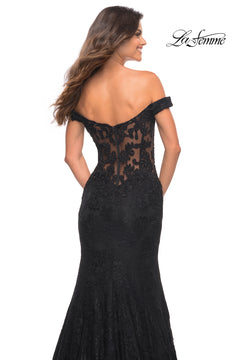 A woman faces away from the camera in the La Femme Off-the-Shoulder Long Lace Prom Dress—an elegant black, floor-length gown with a sheer back and embroidered lace details. The La Femme logo appears in the top right corner.