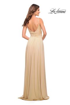A woman models the La Femme Simple Elegant Long Formal Prom Dress—a sleeveless light gold gown with a deep V-back and ruched waist—standing and facing away. The "La Femme" logo is visible in the top right corner.