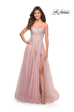A woman wears the Corset-Back Long La Femme A-Line Prom Dress, a light pink floor-length gown with thin straps, a fitted bodice, and a high slit, as she smiles against a white background.