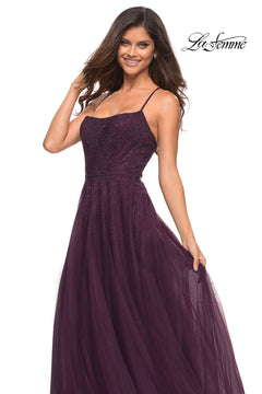 A woman smiles in a sleeveless, floor-length dark purple Corset-Back Long La Femme A-Line Prom Dress with thin straps and a tulle skirt. The "La Femme" logo is displayed in the top right corner.